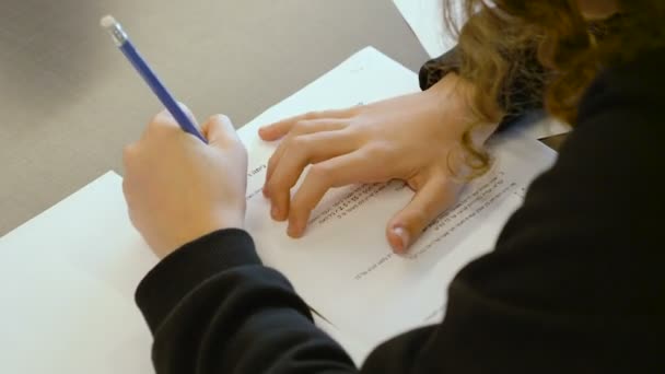 pequeña muchacha talentosa adolescente caucásica israelí tomando una prueba en una clase de escuela primaria. Ella trata de resolver el examen y escribir sus respuestas en papel. OTS de cerca en sus manos y la pluma
. - Imágenes, Vídeo