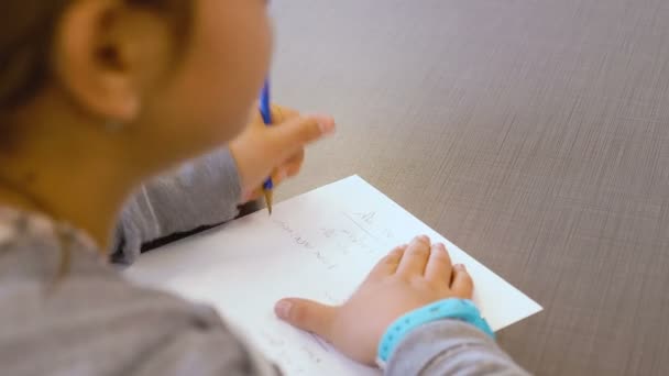 pequeña muchacha talentosa adolescente caucásica israelí escribe en un cuaderno en una clase de escuela primaria. Ella trata de resolver el ejercicio y escribir sus respuestas en papel. OTS de cerca en sus manos y un lápiz
. - Imágenes, Vídeo