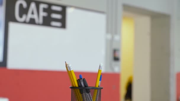 Close up on a metal black box with pencils and pens in the classroom. "Back to school" and education concept. Selective focus and copy space. A blur word "cafe" appears on the board in the background. - Footage, Video