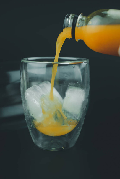 Pouring orange juice on a glass on black background - Photo, Image