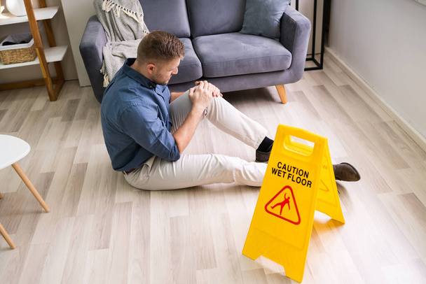 Man Falling On Wet Floor In Front Of Caution Sign At Home - Foto, Imagen