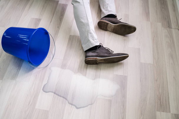 Man Falling On Wet Floor In Front Spilled Bucket Of Water At Home - Фото, изображение