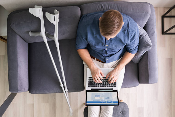 Man With Leg Injury Sitting On Sofa Using Laptop - Foto, afbeelding