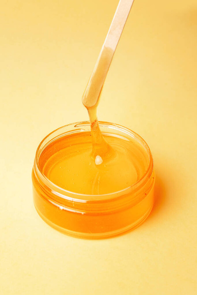 Honey in a jar on a yellow background flows, spatulas for depilation, natural wax for depilation - Photo, image