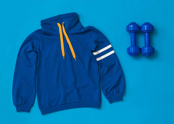 Blaue Hanteln und eine blaue Sportjacke auf hellblauem Hintergrund. - Foto, Bild