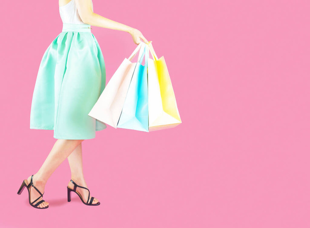 woman low body part wore blue skirt and black high heels. Carrying a shopping bag in many pastel colors on pink background selective focus - Фото, изображение