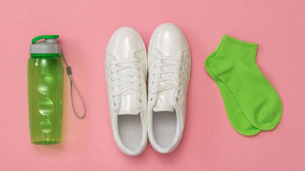 Weiße Turnschuhe, grüne Socken und eine grüne Sportflasche auf rotem Hintergrund. Eine Reihe von Sport-Accessoires. - Foto, Bild