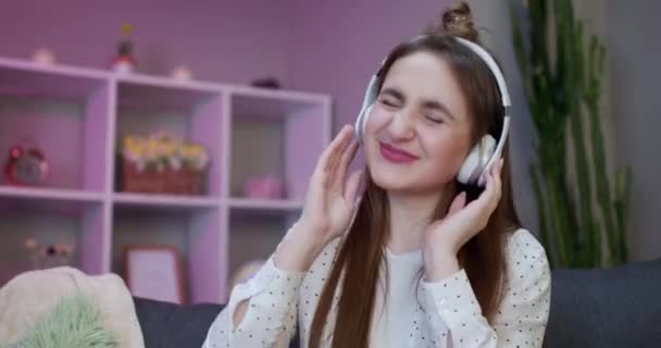 Young beautiful woman in bright outfit enjoying the music at home. Attractive schoolgirl listening music through headphones, eyes closed - Footage, Video