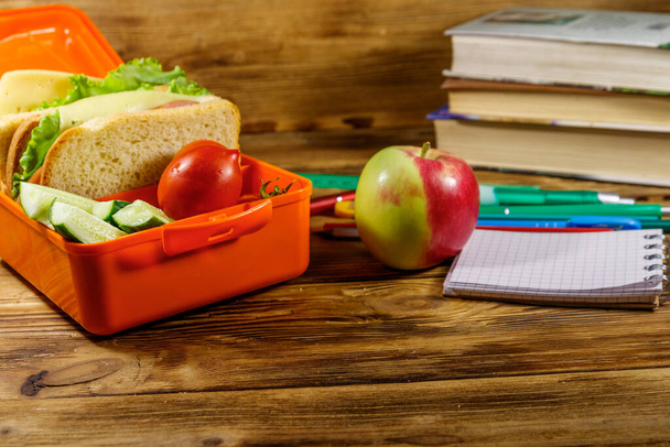 Back to school concept. School supplies, books, apple and lunch box with sandwiches and fresh vegetables on a wooden desk - Photo, image