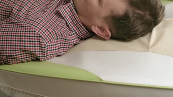 Bir adam masaj yatağında yeşil bigudilerle yatıyor.. - Video, Çekim