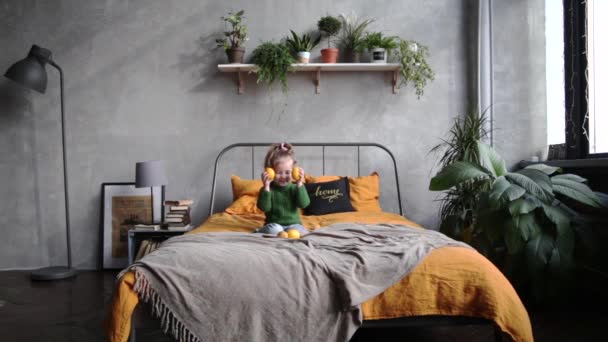 Kleines Mädchen in grünen Klamotten und Jeans spielt mit einer Zitrone auf dem Bett. Zeitlupenvideo - Filmmaterial, Video