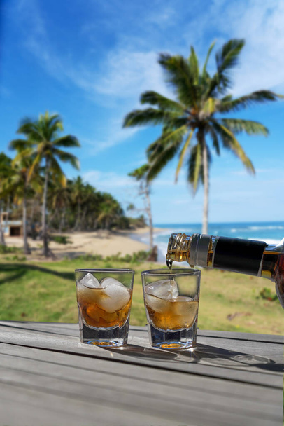 Bebe para dos en una playa caribeña. Dos vasos de licor para un concepto de vacaciones sin preocupaciones para una pareja - Palmeras extendidas sobre el mar
. - Foto, Imagen