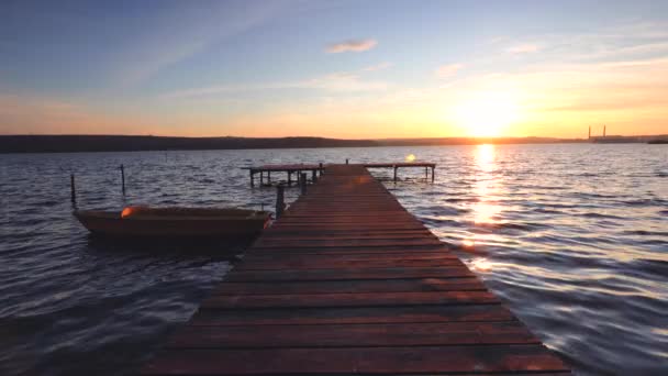 Łódź i drewniany pomost na jeziorze z odbiciem w wodzie o zachodzie słońca - Materiał filmowy, wideo
