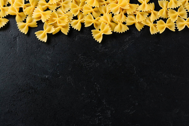 Farfalle raw pasta on black concrete background. Cooking concept. Top view with copy space. - Фото, изображение
