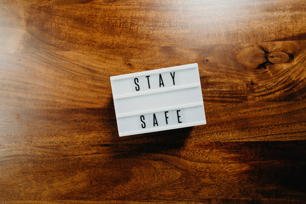 'Blijf veilig' tekst in lichtbak op houten achtergrond. - Foto, afbeelding