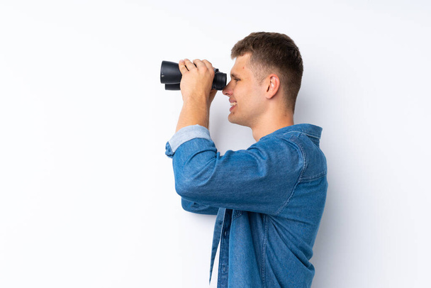 Joven hombre guapo sobre fondo blanco aislado con binoculares negros - Foto, Imagen