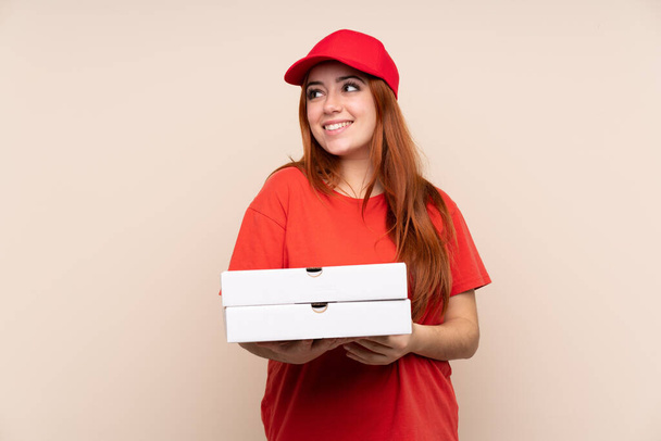 Pizzabote Teenager Mädchen hält eine Pizza über isoliertem Hintergrund lachend und aufblickend - Foto, Bild