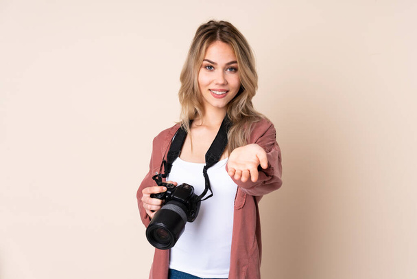 Joven fotógrafa sobre fondo aislado sosteniendo espacio de copia imaginario en la palma de la mano para insertar un anuncio
 - Foto, Imagen