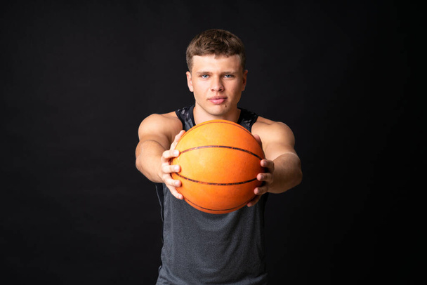 Przystojny młody człowiek gra w koszykówkę nad odizolowaną czarną ścianą - Zdjęcie, obraz