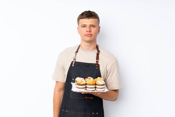 Young handsome man over isolated white background holding mini cakes - 写真・画像