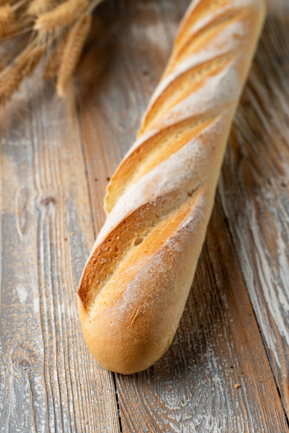 Sourdough francês baguete, assado com crosta crocante dourada, pão branco no fundo de madeira com espigas de trigo em torno de perto
 - Foto, Imagem