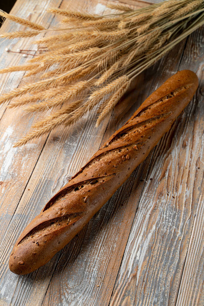 Whole grain rye baguette with seeds and sesame on wooden background with spikes around - Фото, зображення