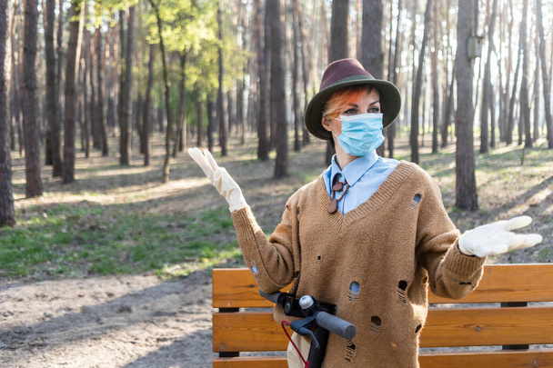Una mujer elegante con máscara y guantes para defenderla de coronavirus. Uso de scooter eléctrico en la ciudad y el parque para estar a salvo
. - Foto, imagen