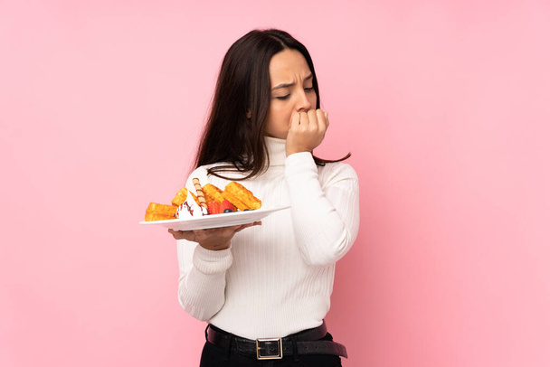 Young brunette woman holding waffles over isolated pink background having doubts - Photo, Image