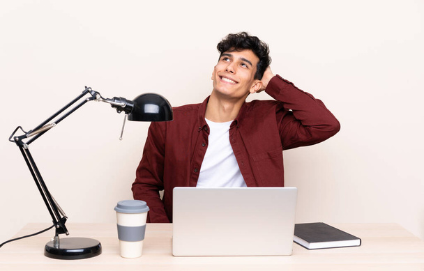 Genç Arjantinli bir adam iş yerinde dizüstü bilgisayarla gülüyor. - Fotoğraf, Görsel