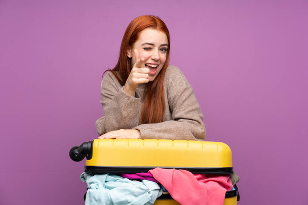 Cestovatel teenager dívka s kufrem plným oblečení ukazuje prstem na vás - Fotografie, Obrázek