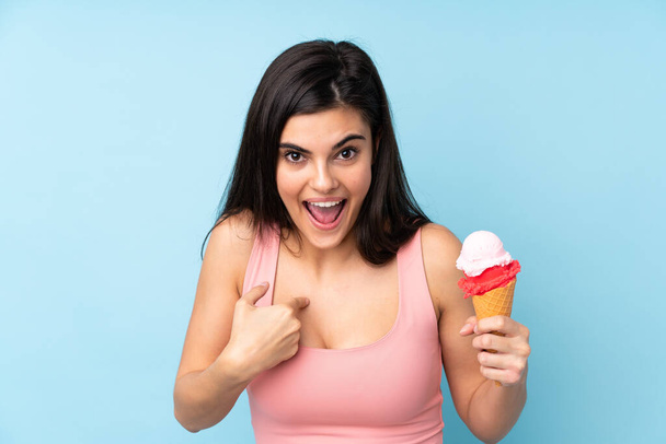 Young woman holding a cornet ice cream over isolated blue background with surprise facial expression - Zdjęcie, obraz