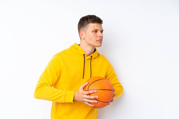 Jonge knappe man over geïsoleerde witte achtergrond met bal van basketbal - Foto, afbeelding