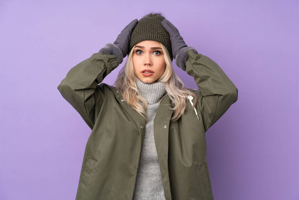 Adolescente blonde avec chapeau d'hiver sur fond violet isolé frustré et prend les mains sur la tête
 - Photo, image