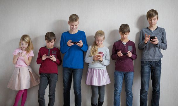 Kinderen staan samen in iedereen met behulp van hun eigen mobiele telefoon - Foto, afbeelding
