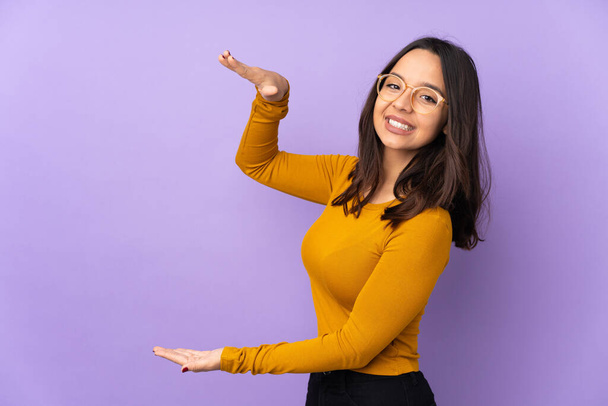 Young mixed race woman isolated on purple background holding copyspace to insert an ad - Foto, Bild