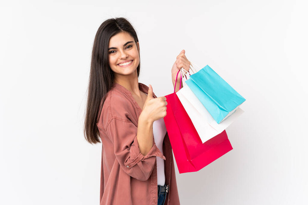 Young woman over isolated white background holding shopping bags and with thumb up - Fotoğraf, Görsel
