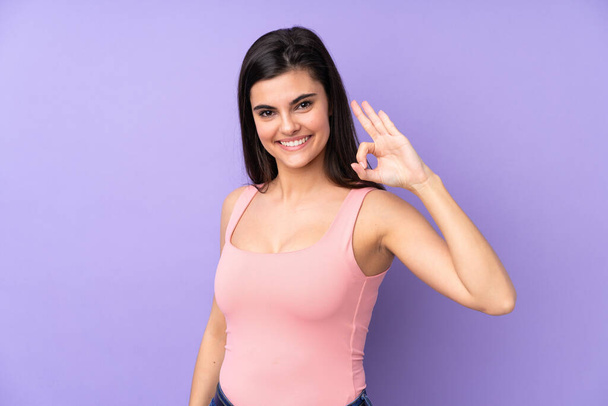 Young woman over isolated purple background showing ok sign with fingers - Photo, image