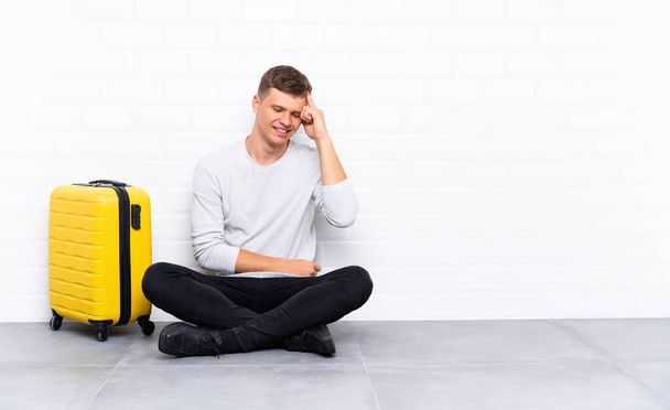 Mladý pohledný muž sedící na podlaze s kufříkem smějícím se - Fotografie, Obrázek