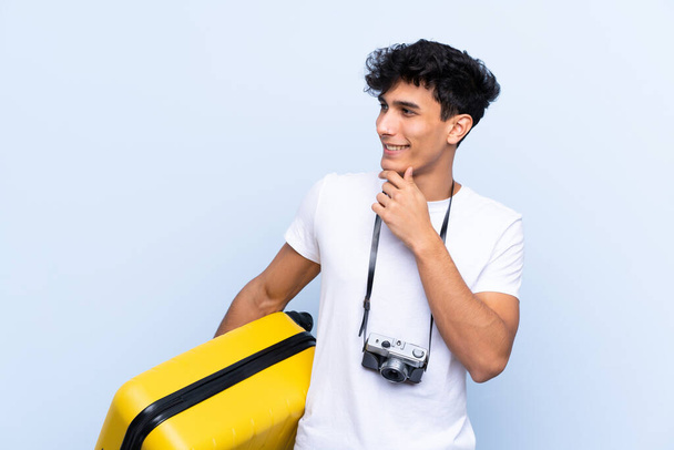 Νεαρός Αργεντινός ταξιδιώτης πάνω από απομονωμένο μπλε φόντο σκέφτεται μια ιδέα και ψάχνει πλευρά - Φωτογραφία, εικόνα