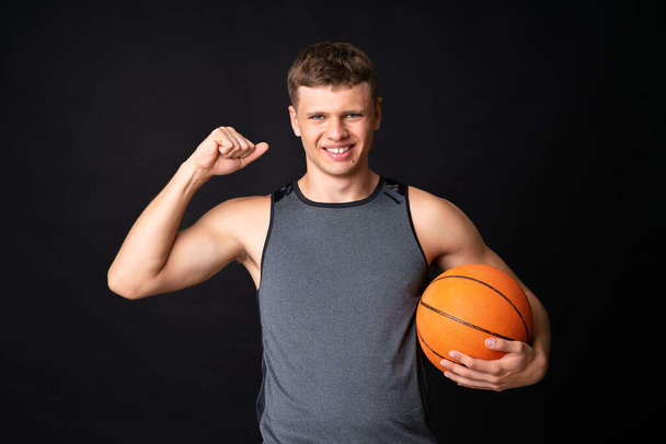Hezký mladý muž hraje basketbal přes izolovanou černou zeď - Fotografie, Obrázek