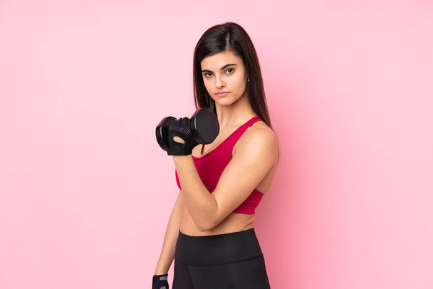 Jonge sport vrouw over geïsoleerde roze achtergrond maken gewichtheffen - Foto, afbeelding