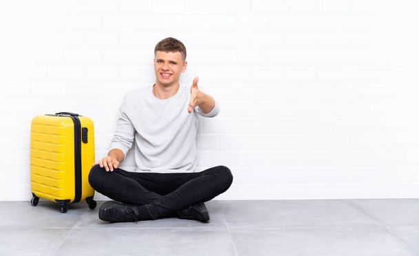 Young handsome man sitting on the floor with a suitcase handshaking after good deal - Fotografie, Obrázek