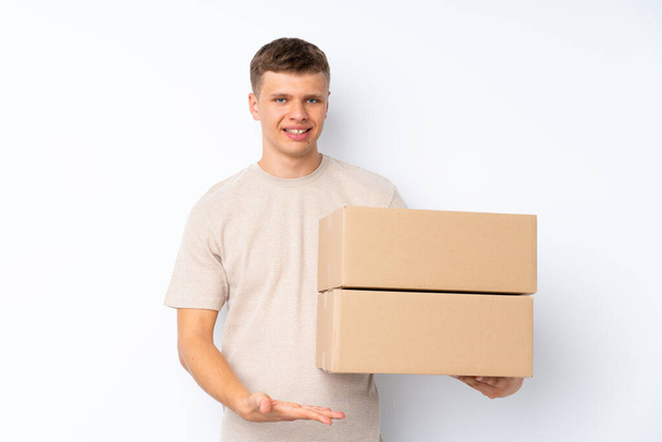 Νεαρός όμορφος άντρας πάνω από απομονωμένο λευκό φόντο κρατώντας ένα κουτί για να το μετακινήσετε σε άλλη τοποθεσία - Φωτογραφία, εικόνα