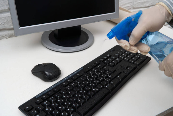 concept of cleaning or disinfecting the office - a businessman cleans the workplace, computer, desk, uses a spray gun and paper napkins. Cleaning surfaces from microbes, viruses and dirt. - Photo, Image