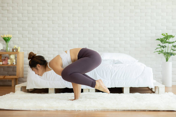 Mujer atlética asiática practica yoga Baby Crow o Baby Bakasana posan para meditar en el dormitorio después de despertarse por la mañana sintiéndose tan cómoda y relajada, Healthcare Concept
 - Foto, Imagen