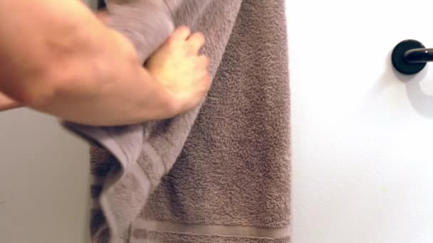 Primer plano de un hombre caucásico extendiendo sus brazos y secándose las manos mojadas sobre una toalla de baño verde colgada en una barra de toallas en una pared de su residencia
. - Metraje, vídeo