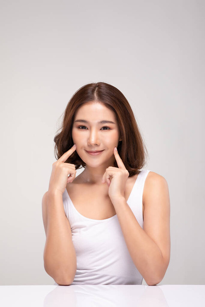 Beautiful Asian young woman touching soft cheek smile with clean and fresh skin Happiness and cheerful with positive emotional,isolated on gray background,Beauty and Cosmetics Concept - Фото, зображення