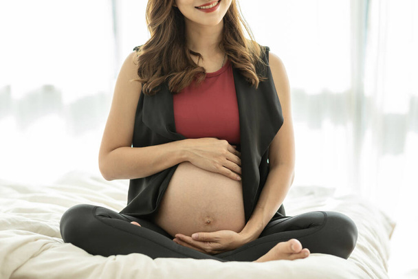 Happy Beautiful Attractive Pregnant Asian Woman sitting on bed smile and holding her big belly feeling so proud and love,Pregnant Healthcare Concept - Photo, Image