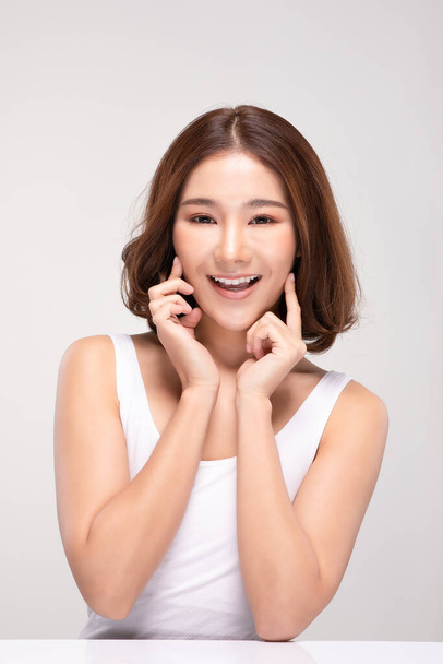Beautiful Asian young woman touching soft cheek smile with clean and fresh skin Happiness and cheerful with positive emotional,isolated on gray background,Beauty and Cosmetics Concept - Foto, imagen