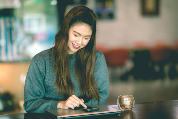 Kahve dükkanında akıllı telefon kullanan güzel Asyalı iş kadını sosyal medya ve internet alışverişi ile gülümseme ve mutluluk, Sıcak Ton - Fotoğraf, Görsel